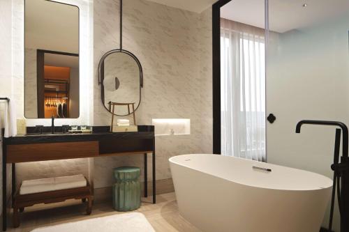 een badkamer met een bad, een wastafel en een spiegel bij Canopy By Hilton Hangzhou Jinsha Lake in Hangzhou