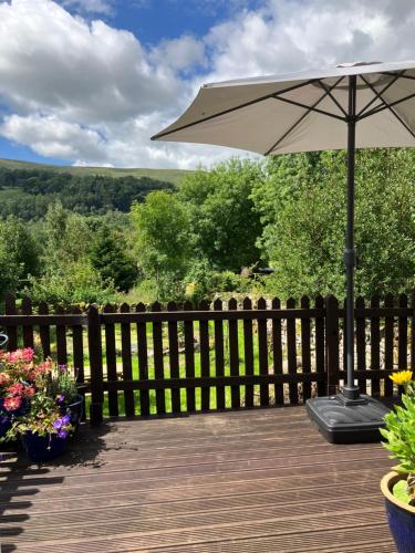 a wooden deck with an umbrella and some flowers at The Dale at Greystones - Luxurious annexe with stunning view in Buckden