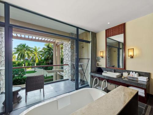 Hilton Sanya Yalong Bay Resort & Spa في سانيا: حمام مع حوض استحمام وشرفة مطلة
