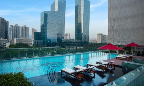 a swimming pool with chairs and umbrellas on a building at Hilton Shenzhen Futian, Metro Station at Hotel Front Door, Close to Futian Convention & Exhibition Center in Shenzhen