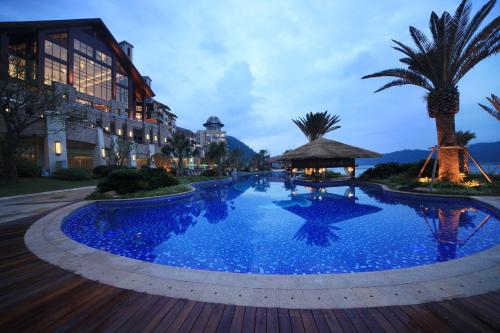 einem großen blauen Pool mit Palmen und einem Gebäude in der Unterkunft Hilton Hangzhou Qiandao Lake Resort in Thousand Island Lake