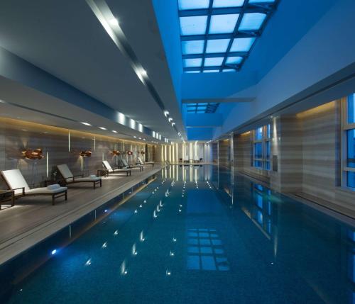 a pool in a building with chairs and tables at Hilton Zhengzhou in Zhengzhou