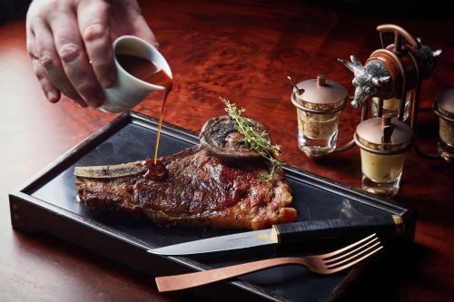 a person pouring sauce on a steak on a tray at Waldorf Astoria Bangkok in Bangkok