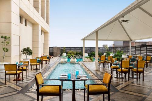 patio z basenem, stołami i krzesłami w obiekcie Hilton Jaipur w mieście Dżajpur