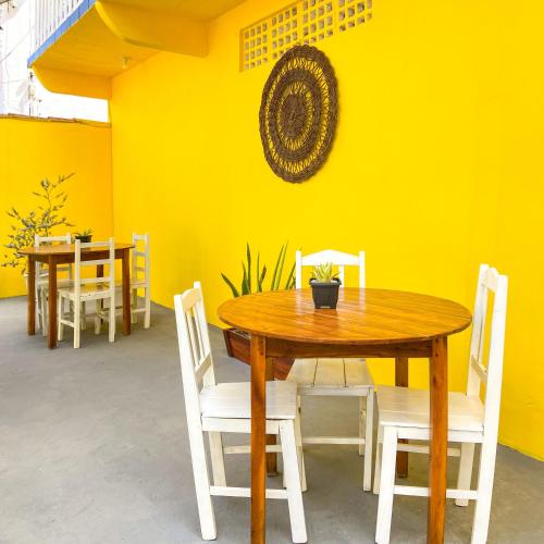 a wooden table with white chairs and a yellow wall at Encanto do Sol Hospedagem in Icaraí
