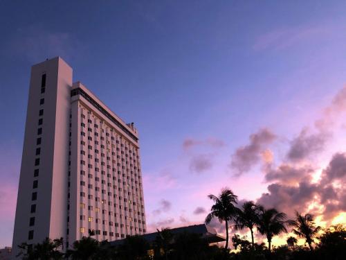 un edificio alto con palmeras frente a la puesta de sol en DoubleTree by Hilton Hotel Naha Shuri Castle, en Naha