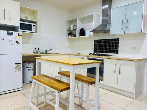 a kitchen with white cabinets and a wooden table and stools at Bundled Bliss 2 bedroom Condo in Adelaide CBD in Adelaide