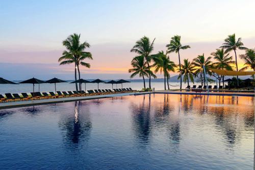 a pool with palm trees and umbrellas and the ocean at Hilton Fiji Beach Resort and Spa in Denarau