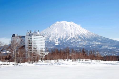 Hilton Niseko Village في نيسيكو: جبل مغطى بالثلج وامامه مبنى