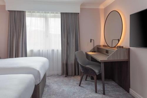 a hotel room with a desk and a bed and a mirror at DoubleTree by Hilton Bath in Bath