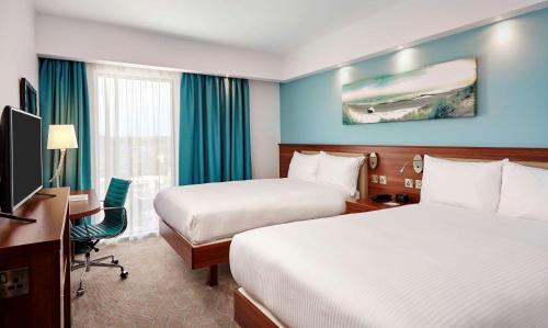 a hotel room with two beds and a desk and a television at Hampton by Hilton Bournemouth in Bournemouth