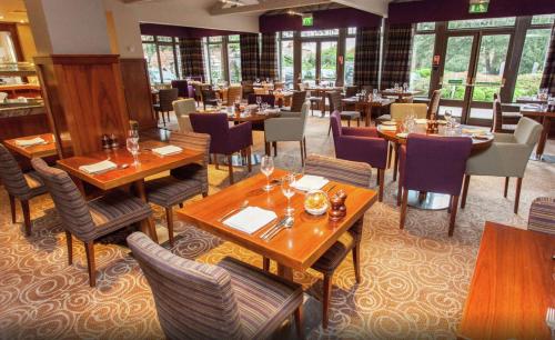 ein Restaurant mit Holztischen, Stühlen und Fenstern in der Unterkunft DoubleTree by Hilton Stratford-upon-Avon, United Kingdom in Stratford-upon-Avon