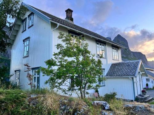 a white house with a mountain in the background at Det Gamle Hotellet Guesthouse in Reine