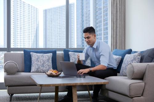 a man sitting on a couch with a laptop at Four Points by Sheraton Surabaya, Pakuwon Indah in Surabaya
