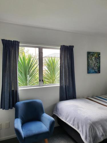 ein Schlafzimmer mit einem Bett, einem blauen Stuhl und einem Fenster in der Unterkunft Alice House in Auckland