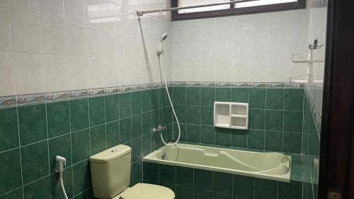 La salle de bains est pourvue de carrelage vert, de toilettes et d'une baignoire. dans l'établissement Green Hill Resort Kemuning, à Panyaweuyan