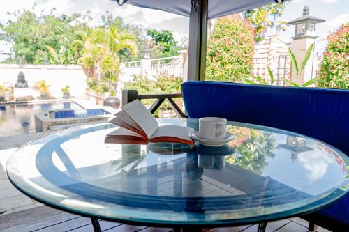 a glass table with a book and a cup of coffee at Villa Tentram Jimbaran by Bali Cabin in Jimbaran