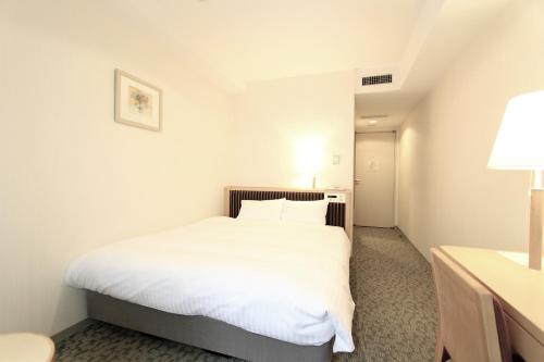 a hotel room with a white bed and a lamp at KOKO HOTEL Sendai Station South in Sendai