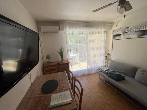 a living room with a table and a large flat screen tv at Studio climatisé avec jardin et plage à 250m in Saint-Mandrier-sur-Mer