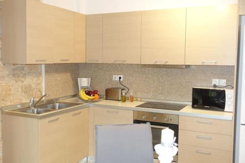 a kitchen with wooden cabinets and a sink and a microwave at Miss Nefeli - Marvelous Stone Apartment in Perdika-Aegina in Aegina Town