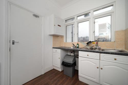 una cocina con armarios blancos, fregadero y ventanas en Flexistay Norbury Aparthotel, en Londres
