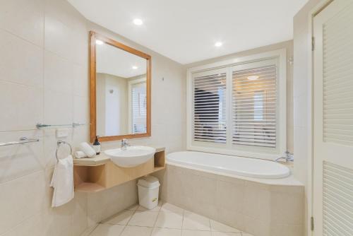 a bathroom with a tub and a sink and a mirror at Quiet Hotel Room in Mantra Salt Beach by uHoliday in Kingscliff