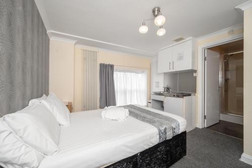 a bedroom with a white bed and a kitchen at Flexistay Tulsi Aparthotel in Croydon