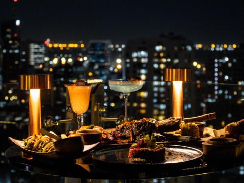 a table with plates of food and drinks and a city at SKYVIEW Hotel Bangkok - Sukhumvit in Bangkok
