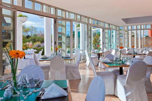 un comedor con mesas, sillas blancas y ventanas en Sheraton Mar Del Plata Hotel en Mar del Plata