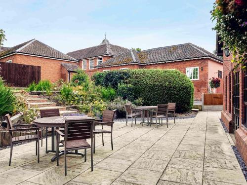 a patio with tables and chairs in a garden at Mercure Shrewsbury Albrighton Hall Hotel & Spa in Shrewsbury