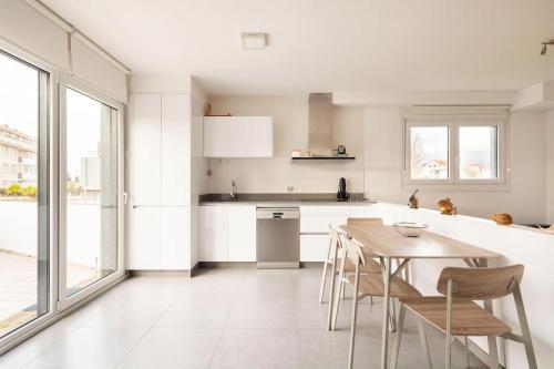 eine weiße Küche mit einem Holztisch und Stühlen in der Unterkunft Apartamento en Baiona con terraza y parking in Pontevedra