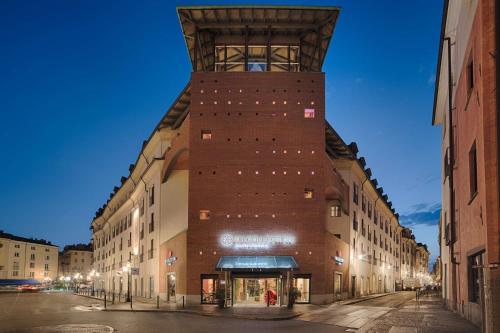 um edifício de tijolos alto com uma torre de relógio numa rua em NH Collection Torino Santo Stefano em Turim