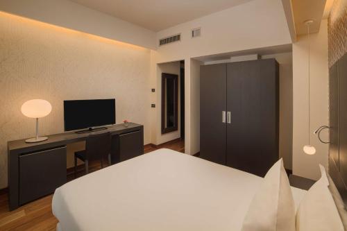 a bedroom with a bed and a desk with a television at NH Collection Torino Santo Stefano in Turin