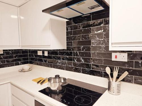 a kitchen with white cabinets and a black tiled wall at Wonderful Apartment in Wembley in London