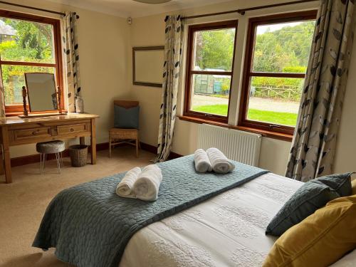 a bedroom with a bed and a desk and windows at The Haven in Saint Fillans