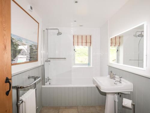 a white bathroom with a sink and a shower at Traeth Ora in Penrhos-Lligwy