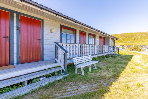 a house with red doors and a bench on the porch at Arctic Lodging North Cape in Skarsvåg