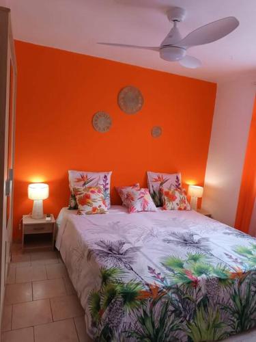 a bedroom with an orange wall and a bed with pillows at Bas de villa (T4) proche de la plage in Bouillante