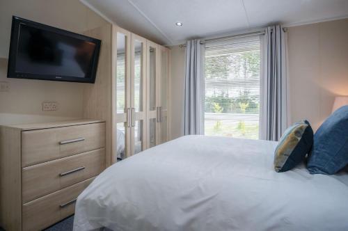 1 Manor Lodge - 3 Bedroom Lodge - Pendine في بينداين: غرفة نوم مع سرير وتلفزيون على الحائط