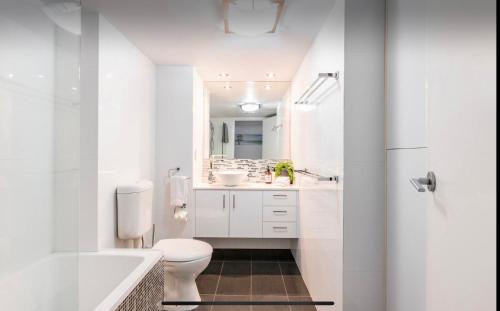 a white bathroom with a toilet and a sink at Beachside Beauty at Burleigh Pavilion! in Gold Coast