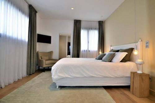 - une chambre avec un grand lit blanc et une chaise dans l'établissement La Villa aux Parasols, à Saint-Laurent-des-Arbres