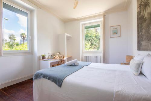 a white bedroom with a large bed and two windows at Far Out Inn in Donostia-San Sebastián