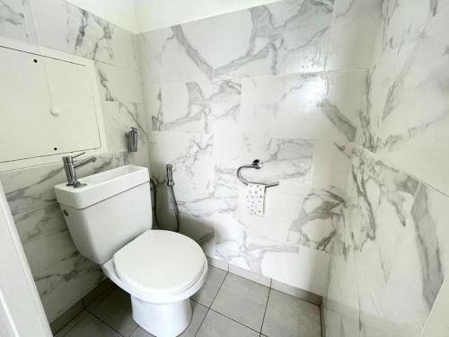 La salle de bains blanche est pourvue de toilettes et de murs en marbre. dans l'établissement Magnifique chambre Avec terrasse (option clim ), à Bagneux