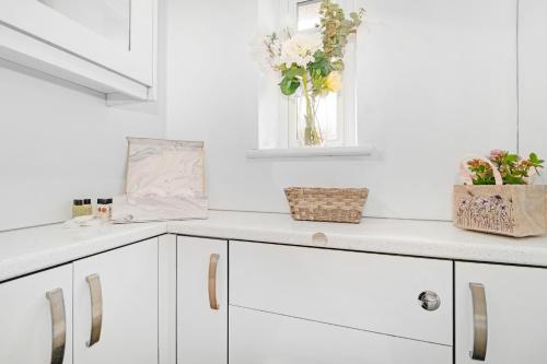 a kitchen with white cabinets and a vase of flowers at Kempton Park Views -Two Double Bedroom Luxury Apartments in Sunbury Common