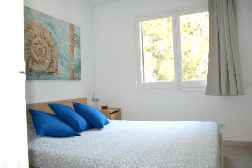 Un dormitorio con una cama con almohadas azules y una ventana en Pianc en Cadaqués