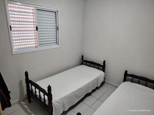 two beds in a white room with a window at Casa da Lu in Barretos