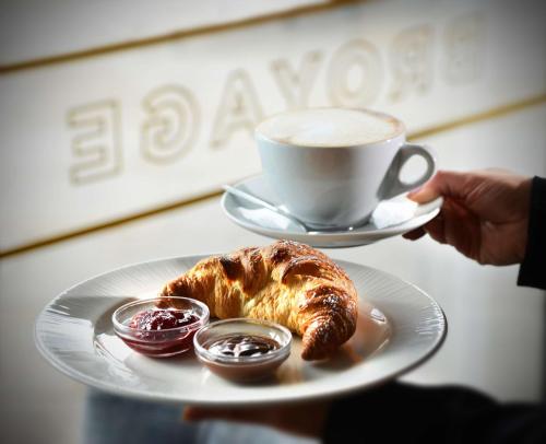 a person holding a plate with a cup of coffee and a pastry at Hilton Dublin Kilmainham in Dublin