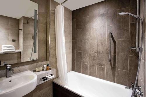 ein Bad mit einer Badewanne, einem Waschbecken und einer Dusche in der Unterkunft Hilton Edinburgh Carlton in Edinburgh