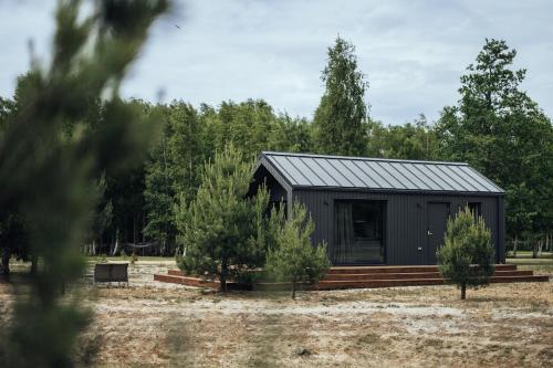 a black cabin in a field with trees at Atpūtas komplekss Pazust Priedēs - SUNSET house in Bernāti