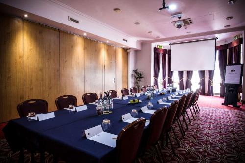 a conference room with a long table with chairs and a screen at DoubleTree by Hilton Cheltenham-Cotswolds in Cheltenham